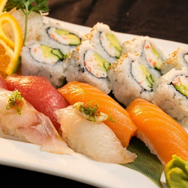 A white plate holds various sushi and sashimi, including California rolls, tuna, and salmon.