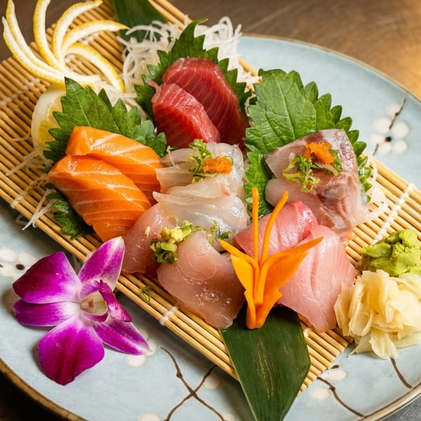 Assorted sashimi platter with tuna, salmon, and white fish, garnished with a purple orchid.