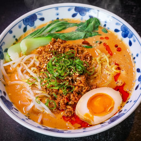 Steaming bowl of tantanmen ramen with minced pork, bok choy, bean sprouts, and a soft-boiled egg.