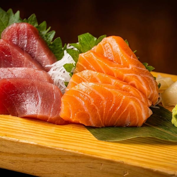 Fresh tuna and salmon sashimi slices with wasabi and pickled ginger on a wooden board.