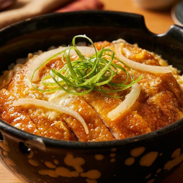 A close-up of a katsudon bowl with crispy fried pork cutlet, egg, onions, and green onions.