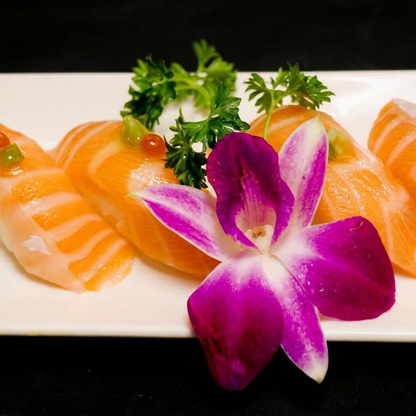 Four pieces of salmon nigiri sushi with green and red toppings, garnished with parsley and an orchid.