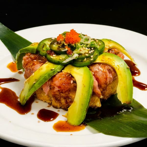 Sushi dish with avocado slices, jalapeños, and orange roe on a white plate with sauce.