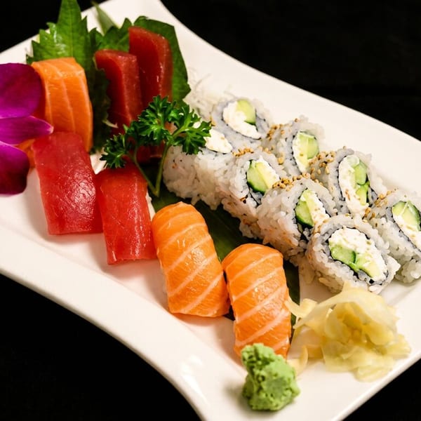A white plate with various sushi, sashimi, and rolls, garnished with an orchid and parsley.